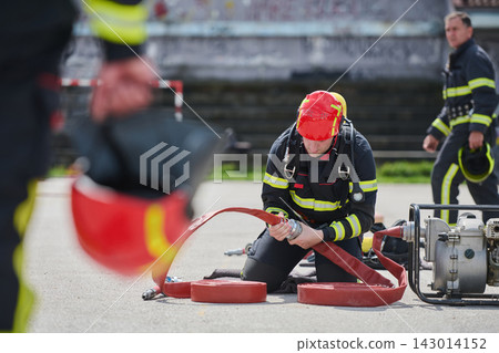 Firefighter Connecting Fire Hose During Training Exercise With Protective Helmet and Gear 143014152