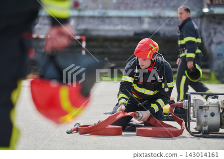Firefighter Preparing Hose During Rescue Training Exercise With Team In Full Gear On Pavement Firefighter Preparing Hose During Rescue Training Exercise With Team In Full Gear On Pavement 143014161