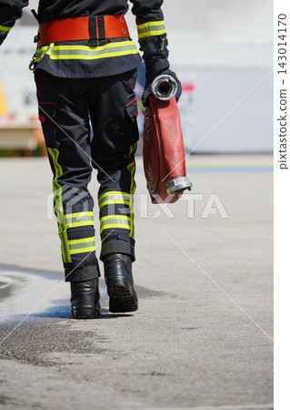 Firefighter Carrying Red Fire Hose In Protective Uniform With Reflective Stripes Walking Away Firefighter Carrying Red Fire Hose In Protective Uniform With Reflective Stripes Walking Away 143014170