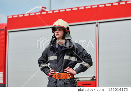 Young Firefighter Standing Confidently In Front Of Red Fire Truck Wearing Helmet And Gear Young Firefighter Standing Confidently In Front Of Red Fire Truck Wearing Helmet And Gear 143014173