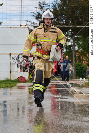 Firefighter Running With Hose And Manifold During Emergency Response Training Near Fire Truck Firefighter Running With Hose And Manifold During Emergency Response Training Near Fire Truck 143014174