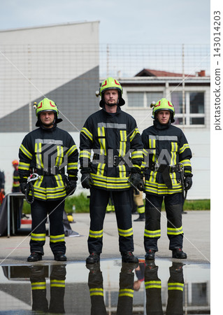 Three Firefighters Standing Together in Protective Gear With Helmets and Puddle Reflection Three Firefighters Standing Together in Protective Gear With Helmets and Puddle Reflection 143014203