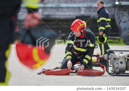 Firefighter Preparing Hose and Gear During Emergency Training With Red Helmet and Pump Equipment Firefighter Preparing Hose and Gear During Emergency Training With Red Helmet and Pump Equipment 143014207
