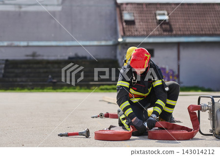 Firefighter Preparing Hose During Outdoor Training Exercise Wearing Protective Gear And Red Helmet Firefighter Preparing Hose During Outdoor Training Exercise Wearing Protective Gear And Red Helmet 143014212