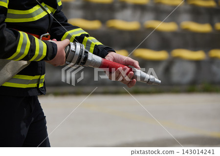 Firefighter Holding Fire Hose Nozzle During Training Drill With Protective Uniform and Reflective Stripes Firefighter Holding Fire Hose Nozzle During Training Drill With Protective Uniform and Reflective Stripes 143014241