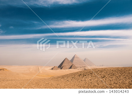 Pyramids of Giza wide landscape panorama across golden sandy desert under dramatic blue sky with sweeping copy space ideal for travel editorial and Pyramids of Giza wide landscape panorama across golden sandy desert under dramatic blue sky with sweeping copy space ideal for travel editorial and 143014243