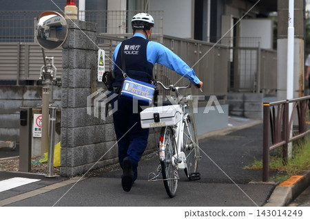 Police officer walking while pushing a bicycle 143014249