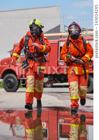 Two Firefighters In Full Protective Gear Running Toward Emergency Near Fire Truck Two Firefighters In Full Protective Gear Running Toward Emergency Near Fire Truck 143014285