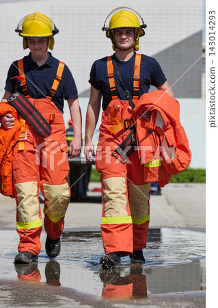 Two Firefighters in Orange Turnout Gear Walking Through Puddle After Training Exercise Two Firefighters in Orange Turnout Gear Walking Through Puddle After Training Exercise 143014293