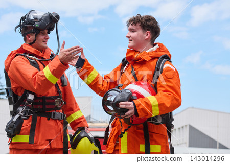 Two Firefighters In Orange Protective Gear Celebrating Teamwork After Training With Helmets And Breathing Apparatus Two Firefighters In Orange Protective Gear Celebrating Teamwork After Training With Helmets And Breathing Apparatus 143014296