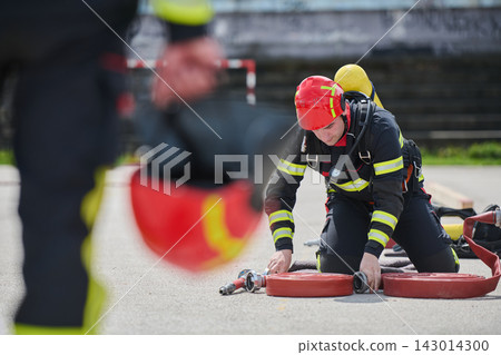 Firefighter Training Drill With Helmeted Firefighter Rolling Hoses and Preparing Equipment for Rescue Firefighter Training Drill With Helmeted Firefighter Rolling Hoses and Preparing Equipment for Rescue 143014300