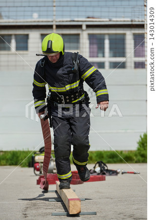 Firefighter Training Exercise Balancing On Beam While Carrying Fire Hose In Protective Gear Firefighter Training Exercise Balancing On Beam While Carrying Fire Hose In Protective Gear 143014309