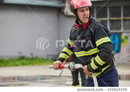 Firefighter Handling Fire Hose Wearing Helmet And Protective Gear During Emergency Training Exercise Firefighter Handling Fire Hose Wearing Helmet And Protective Gear During Emergency Training Exercise 143014339