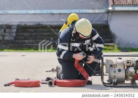 Firefighter Preparing Hose and Portable Pump Equipment While Kneeling During Training Or Response 143014352