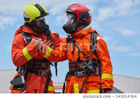 Two Firefighters in Orange Protective Gear and Helmets Showing Teamwork During Emergency Training Two Firefighters in Orange Protective Gear and Helmets Showing Teamwork During Emergency Training 143014364