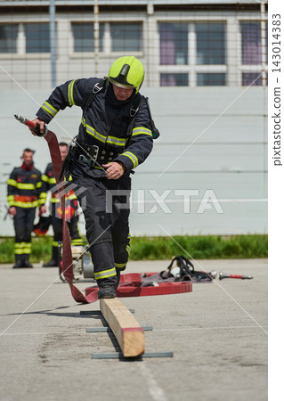 Firefighter Training Drill With Helmeted Firefighter Running With Hose Over Balance Beam During Exercise 143014383
