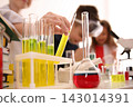 Smart pupils making experiment in chemistry class, focus on flask with reagent 143014391