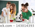 Schoolgirl looking through microscope and her classmates at chemistry class 143014393