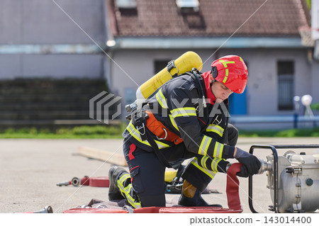 Firefighter Connecting Hose During Training Drill Wearing Protective Gear And Breathing Apparatus Firefighter Connecting Hose During Training Drill Wearing Protective Gear And Breathing Apparatus 143014400