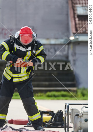 Firefighter In Full Gear Preparing Equipment During Urban Rescue Drill With Red Helmet And Reflective Stripes Firefighter In Full Gear Preparing Equipment During Urban Rescue Drill With Red Helmet And Reflective Stripes 143014402