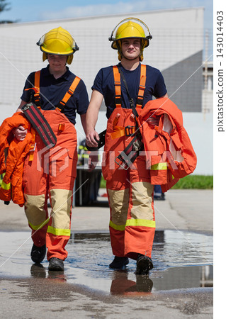 Two Young Firefighters Walking in Orange Turnout Gear During Training Drill at Fire Station 143014403