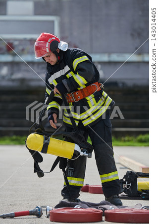 Firefighter Putting On Breathing Apparatus During Training Drill With Hose And Safety Gear Firefighter Putting On Breathing Apparatus During Training Drill With Hose And Safety Gear 143014405