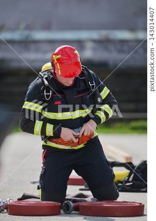 Firefighter in Full Protective Gear Kneeling With Hose Preparing Equipment During Training Firefighter in Full Protective Gear Kneeling With Hose Preparing Equipment During Training 143014407
