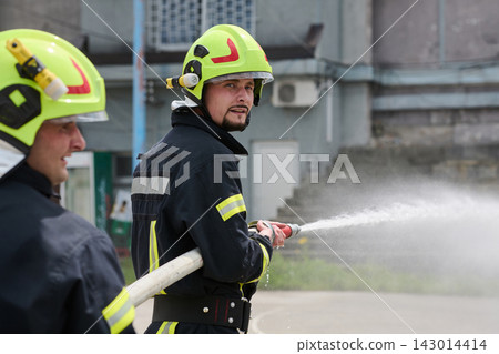 Firefighter Team Using Hose To Spray Water During Training Or Emergency Response Firefighter Team Using Hose To Spray Water During Training Or Emergency Response 143014414