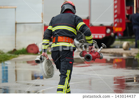 Firefighter Carrying Hose and Fire Hydrant Splitter Near Fire Truck During Emergency Response Training Firefighter Carrying Hose and Fire Hydrant Splitter Near Fire Truck During Emergency Response Training 143014437
