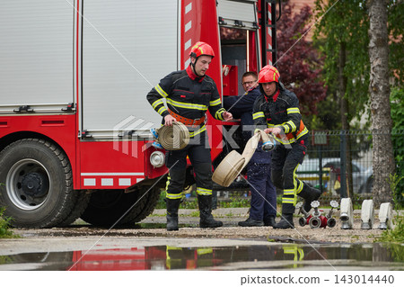 Firefighters Rolling Out Hose From Red Fire Truck During Emergency Response Drill In Urban Setting Firefighters Rolling Out Hose From Red Fire Truck During Emergency Response Drill In Urban Setting 143014440