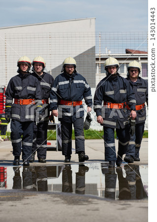 Firefighter Team Walking Together in Uniforms Reflection on Wet Pavement at Training Site Firefighter Team Walking Together in Uniforms Reflection on Wet Pavement at Training Site 143014443