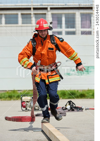 Firefighter In Orange Protective Gear Balancing With Hose During Emergency Training Drill Firefighter In Orange Protective Gear Balancing With Hose During Emergency Training Drill 143014448
