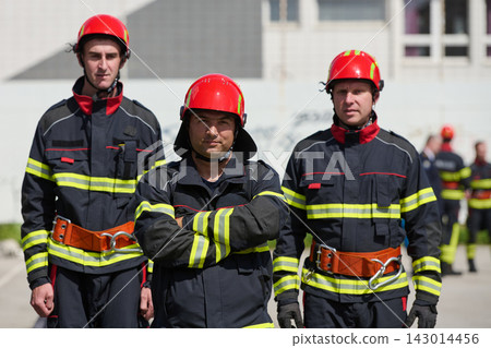 Three Firefighters in Uniform With Red Helmets Standing Confidently During Training Or Emergency Response Three Firefighters in Uniform With Red Helmets Standing Confidently During Training Or Emergency Response 143014456