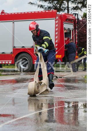 Firefighter Running With Rolled Hose Toward Red Fire Truck During Emergency Response Training Firefighter Running With Rolled Hose Toward Red Fire Truck During Emergency Response Training 143014472