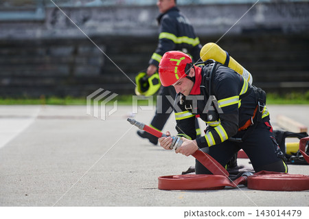 Firefighter Connecting Fire Hose During Training Drill With Helmet And Breathing Apparatus Firefighter Connecting Fire Hose During Training Drill With Helmet And Breathing Apparatus 143014479