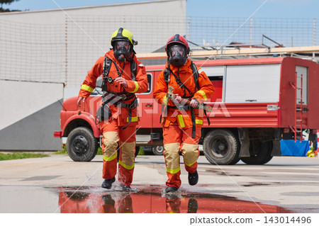 Two Firefighters in Full Protective Gear Running Past Fire Truck During Emergency Response Drill Two Firefighters in Full Protective Gear Running Past Fire Truck During Emergency Response Drill 143014496
