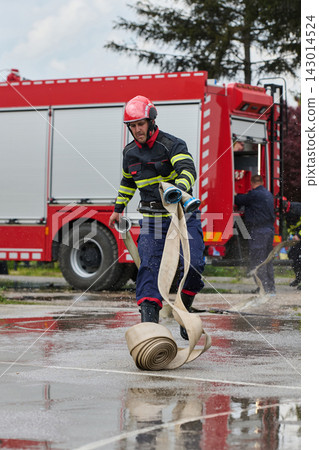 Firefighter Running With Hose In Front Of Red Fire Truck During Emergency Drill Firefighter Running With Hose In Front Of Red Fire Truck During Emergency Drill 143014524
