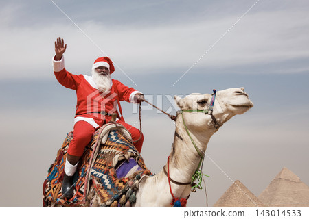 Santa Claus riding a decorated camel and waving joyfully with ancient Giza pyramids rising in the background a playful global Christmas holiday travel Santa Claus riding a decorated camel and waving joyfully with ancient Giza pyramids rising in the background a playful global Christmas holiday travel 143014533