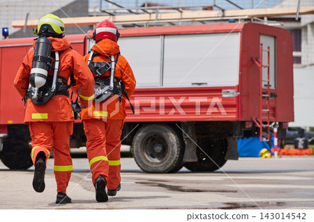 Firefighters in Protective Suits Running Toward Red Fire Truck During Emergency Response Drill Firefighters in Protective Suits Running Toward Red Fire Truck During Emergency Response Drill 143014542