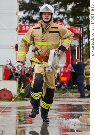 Firefighter Running With Hose And Valve Equipment Carrying Out Emergency Response Near Fire Truck Firefighter Running With Hose And Valve Equipment Carrying Out Emergency Response Near Fire Truck 143014619