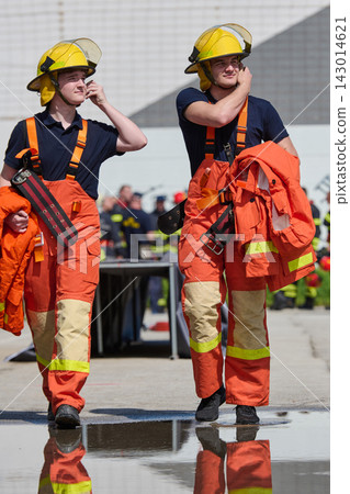 Two Firefighters in Orange Turnout Gear and Yellow Helmets Walking During Training Exercise 143014621