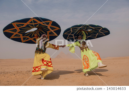 Pair of Egyptian tanoura folk dancers in vivid yellow and lime green costumes hold hands while spinning matching geometric discs before the ancient Pair of Egyptian tanoura folk dancers in vivid yellow and lime green costumes hold hands while spinning matching geometric discs before the ancient 143014633