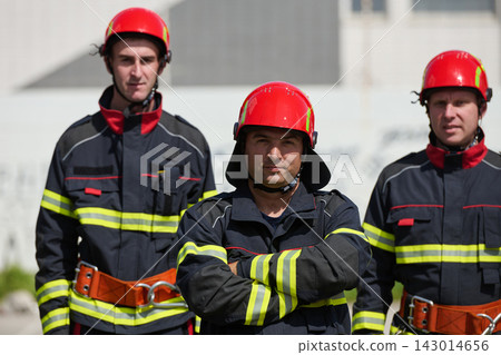 Firefighters Standing Together in Uniform With Red Helmets and Safety Gear Ready for Rescue 143014656