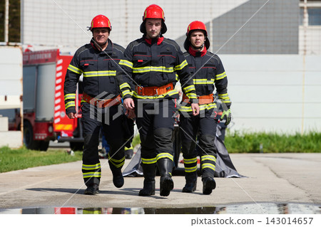 Three Firefighters Walking Confidently in Full Gear With Fire Truck in Background 143014657