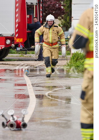 Firefighter Carrying Hose Reels Near Fire Truck During Wet Emergency Response Drill Firefighter Carrying Hose Reels Near Fire Truck During Wet Emergency Response Drill 143014710