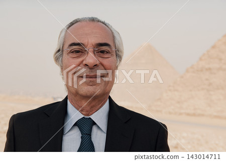 Close up portrait of a composed distinguished senior businessman in dark suit and tie with wire frame glasses smiling before the softly blurred Great Close up portrait of a composed distinguished senior businessman in dark suit and tie with wire frame glasses smiling before the softly blurred Great 143014711