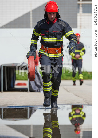 Firefighter Running With Hose During Drill Wearing Helmet And Reflective Protective Gear Firefighter Running With Hose During Drill Wearing Helmet And Reflective Protective Gear 143014715