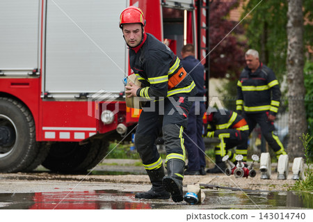 Firefighter Carrying Hose Near Red Fire Truck During Emergency Response And Rescue Operation Firefighter Carrying Hose Near Red Fire Truck During Emergency Response And Rescue Operation 143014740
