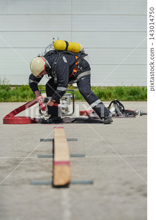 Firefighter In Protective Gear Connecting Hose During Outdoor Training With Air Tank And Helmet 143014750