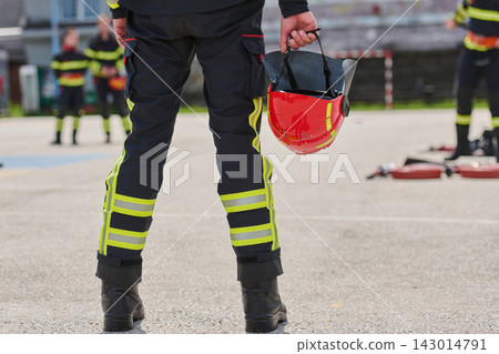 Firefighter Holding Red Helmet During Training Drill With Team In High-Visibility Uniform Firefighter Holding Red Helmet During Training Drill With Team In High-Visibility Uniform 143014791